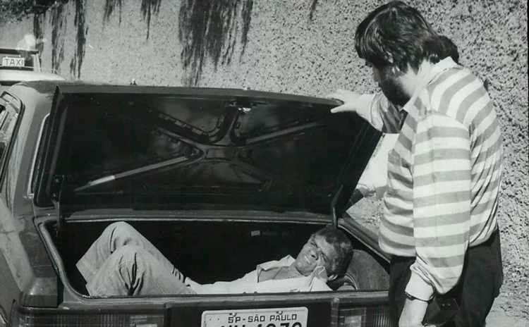 Observado pelo radialista Afanásio Jazadji, Chico Pé de Pato se esconde no porta-malas de um Opala para seguir em segurança até a rádio Capital, nos Jardins – Foto: osé Luis da Conceição - 26.ago.1985/Folhapress