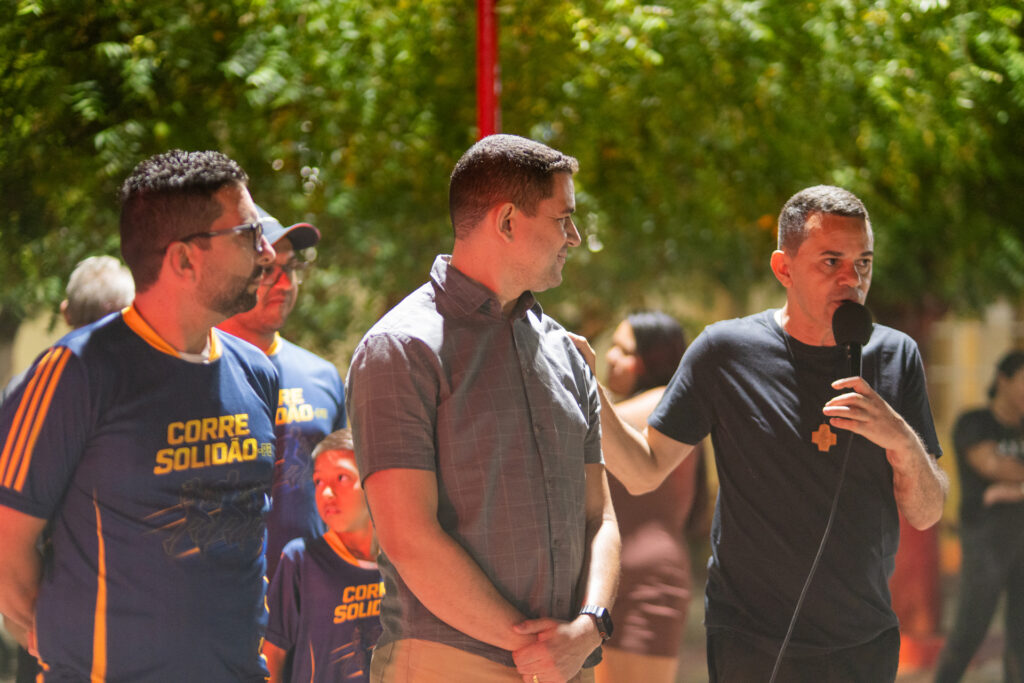 Padre Ayron fala ao microfone ao lado de Tony e do prefeito Mayco Araújo durante o Treinão Corrida dos Milagres.